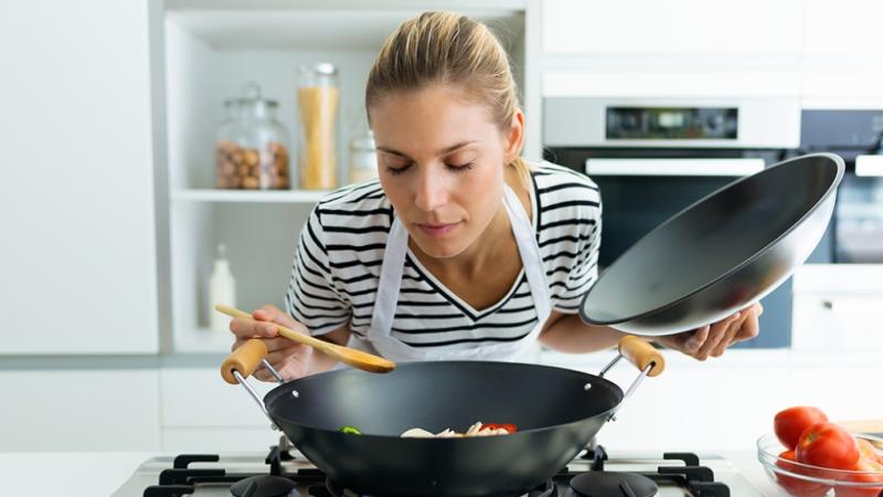 White woman sniffing food she's cooking in a Wok 