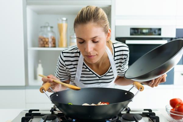 White woman sniffing food she's cooking in a Wok 